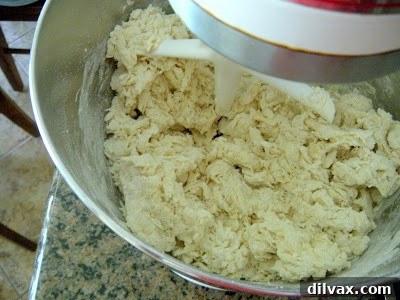 Dough forming in a stand mixer bowl using a paddle attachment, showing its initial shaggy texture.