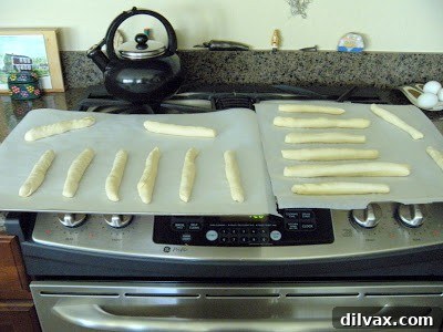 Raw breadstick dough, perfectly shaped and spaced on a parchment-lined baking sheet, after its initial rise.