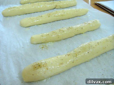 Breadsticks on a baking sheet, brushed with melted butter and sprinkled with seasoning just before going into the oven.