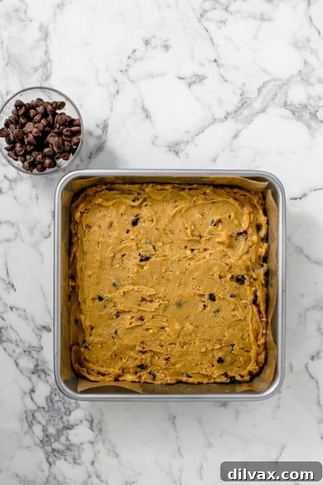 A baking pan filled with unbaked blondie batter, with a bowl of semi-sweet chocolate chips next to it, ready for the oven.