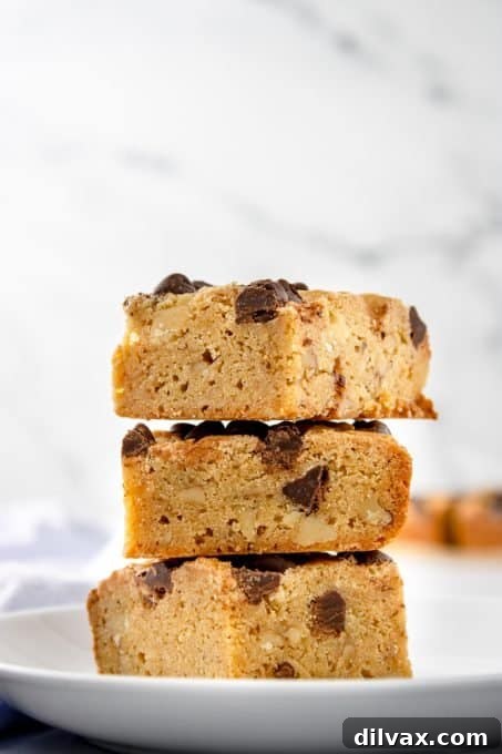 A stack of golden chocolate chip blondies on a cooling rack, with more blondies visible in the background.