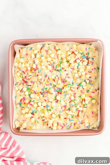Dough with colorful sprinkles spread in a baking pan, topped with the remaining dough pieces, ready for the oven.