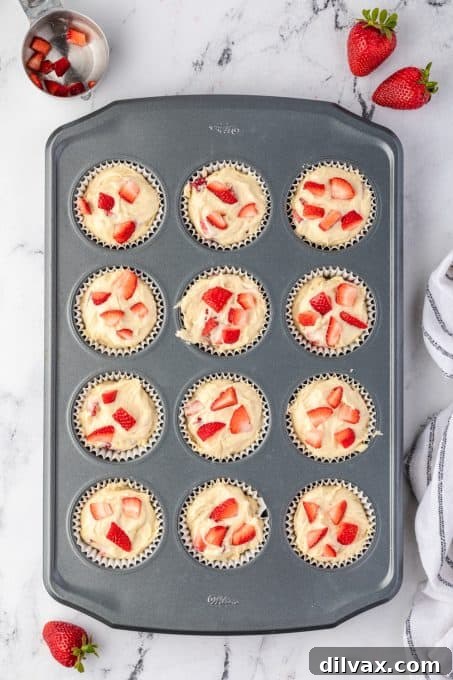 Muffin tin filled with raw batter, topped with fresh strawberry pieces, ready for baking.