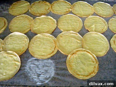 Stack of thin, golden cardamom crepes cooling on wax paper on a kitchen counter.