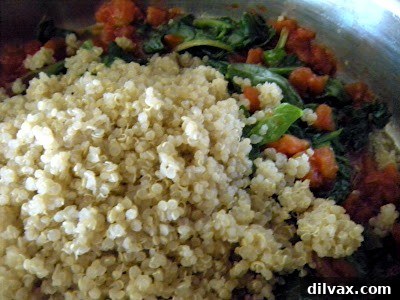 Cooked quinoa being added to the spinach and tomato mixture in the pan.