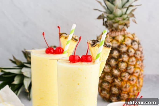 Two glasses filled with a vibrant yellow pineapple coconut rum slush, garnished with pineapple wedges.