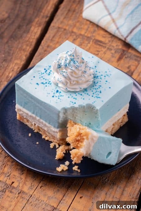 Electric Blue Raspberry Bars 8 A layered no-bake blue dessert with a bite taken out, revealing its distinct cookie crust, cheesecake, and blue raspberry Jello layers.