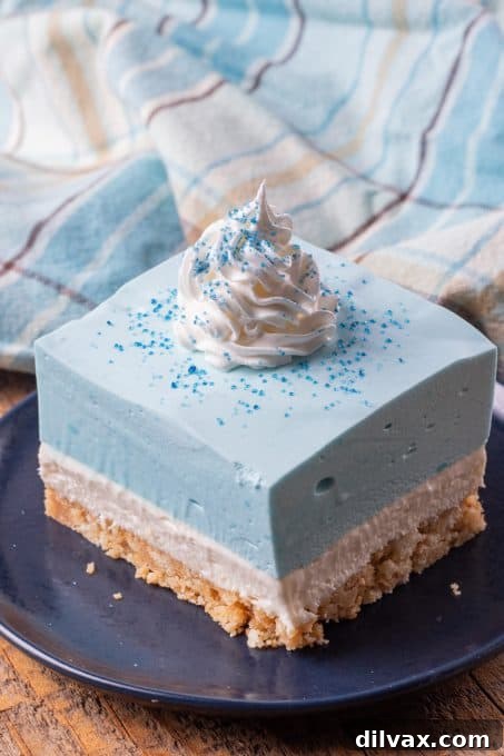 Electric Blue Raspberry Bars 9 A close-up of a perfectly layered cheesecake dessert with a clear blue raspberry Jello layer, inviting a delicious bite.