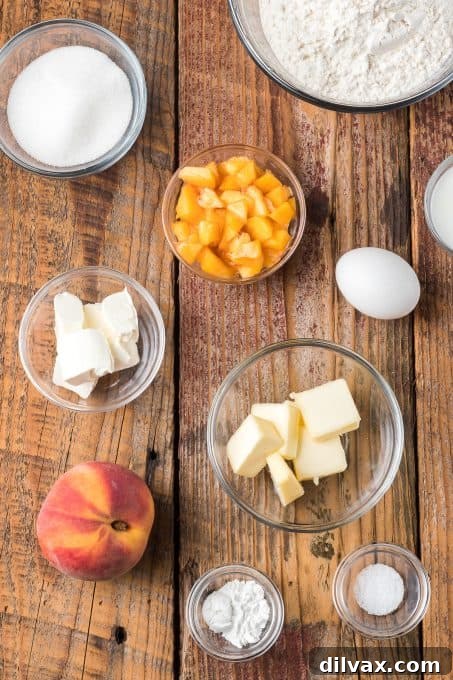 A collection of ingredients laid out on a surface, including flour, sugar, butter, cream cheese, an egg, and a fresh peach, for making peach scones.
