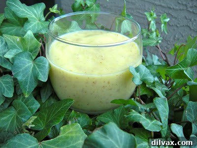 A vibrant yellow and orange pineapple mango smoothie in a clear glass, garnished with a slice of fresh pineapple.