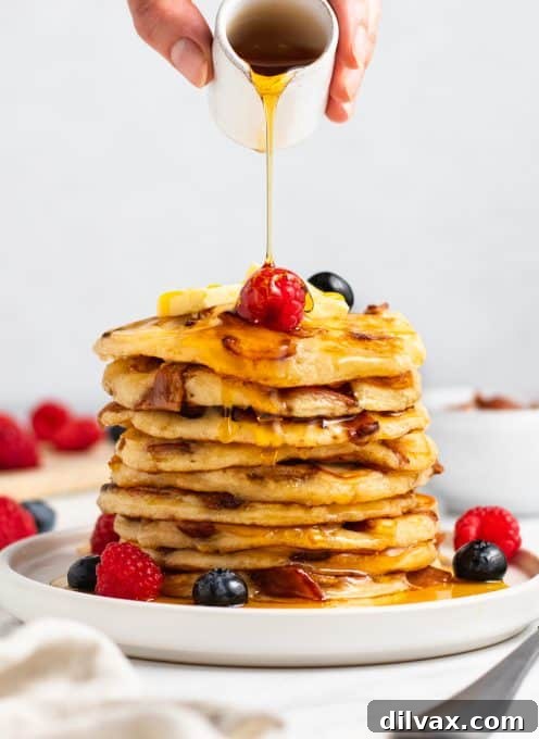Close-up of a stack of fluffy Bacon Pancakes on a white plate, with maple syrup drizzled over.