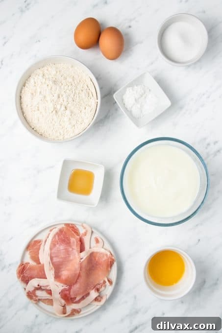 A collection of fresh ingredients laid out on a kitchen counter, including flour, eggs, buttermilk, butter, sugar, vanilla extract, and raw bacon strips, all ready for making homemade bacon pancakes.