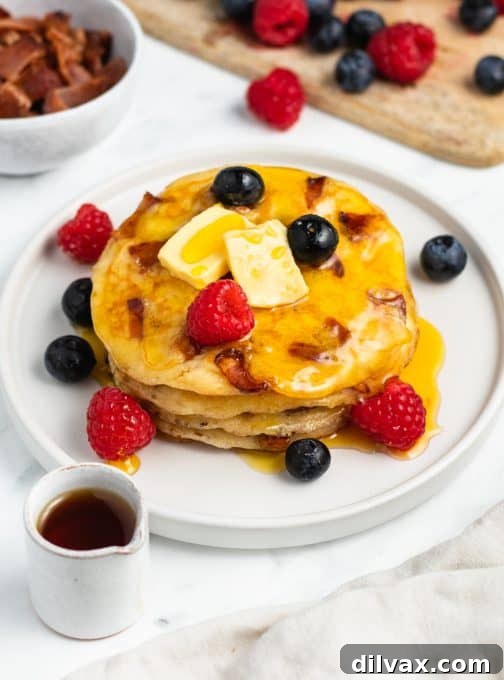 A plate of homemade bacon pancakes, garnished with a pat of butter and a generous amount of maple syrup, ready to be enjoyed.