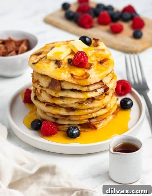 A close-up of a stack of fluffy buttermilk pancakes, with small pieces of crispy bacon visible within the batter, showing the perfect texture and savory inclusions.