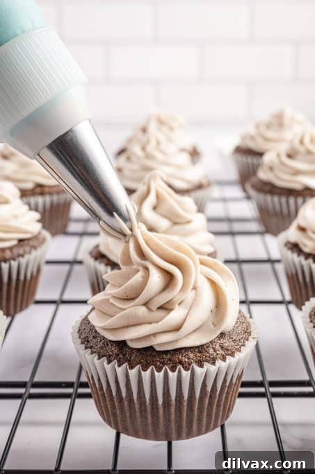A close-up shot of rich Oreo frosting being piped onto a freshly baked chocolate cupcake.