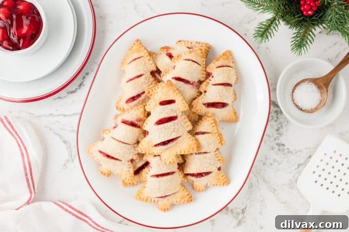 Two festive Christmas Cherry Hand Pies shaped like trees on a wooden surface.