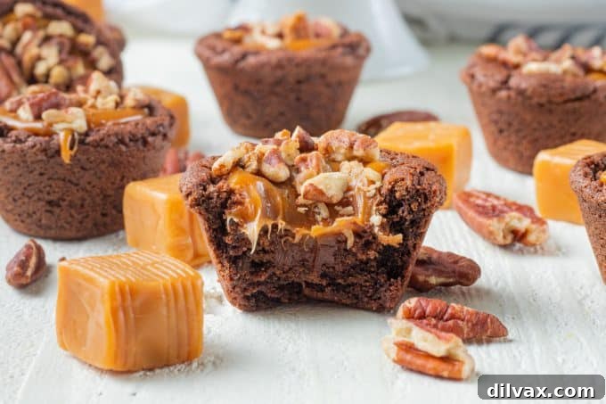 A perfectly baked chocolate cookie cup, filled with molten dark chocolate, luscious caramel, and crunchy pecan pieces. A bite has been taken, revealing the delightful layers.
