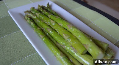 A serving of baked asparagus next to a fork on a plate.