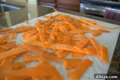 A mandoline slicer in action, demonstrating the safe and effective way to slice carrots thinly.