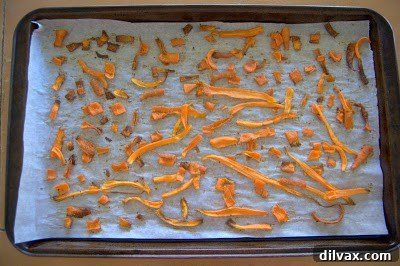 Partially baked carrot chips on a baking sheet, with some pieces showing signs of browning, indicating the need for flipping.