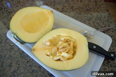 Acorn squash cut in half lengthwise on a cutting board, revealing the seeds and fibrous interior.