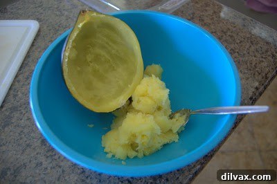 Scooped acorn squash flesh in a bowl next to the hollowed-out squash shell, ready for filling.
