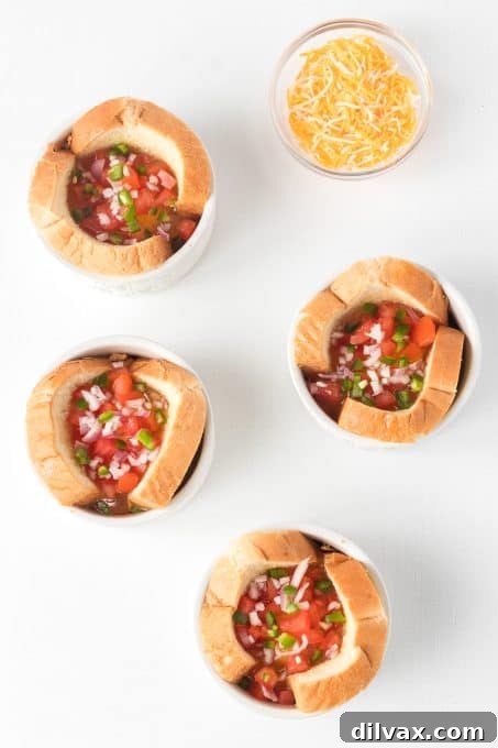 Eggs in bread cups topped with chopped onion and diced tomato before baking.