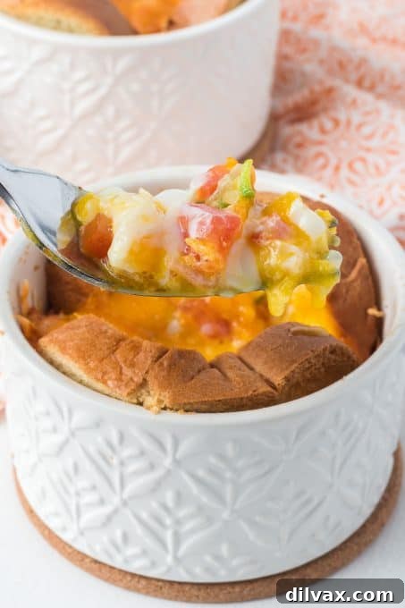 A close-up of a fork holding a bite of baked egg, tomato, onion, and cheese in toast.