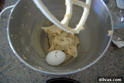 Adding egg and vanilla extract to the creamed butter and sugar mixture.