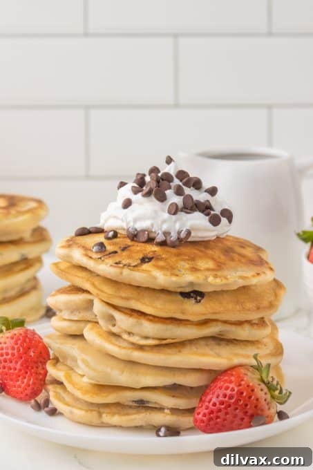 A close-up shot of a stack of fluffy chocolate chip pancakes on a plate, ready to be served.