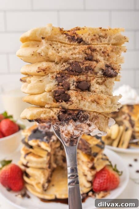 A close-up shot of a fork taking a bite from a fluffy chocolate chip pancake.