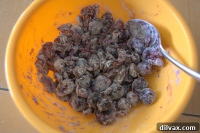 Close-up of fresh blueberries and dried cranberries being tossed with flour in a small bowl, illustrating the technique to prevent fruit from sinking in baked goods.
