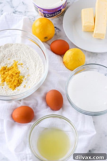 Neatly arranged baking ingredients, including lemons, eggs, butter, flour, and a bowl of ricotta cheese, awaiting preparation.