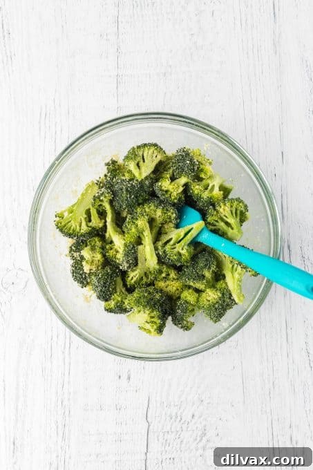 Broccoli florets tossed with olive oil, garlic powder, Parmesan cheese, and salt on a baking sheet