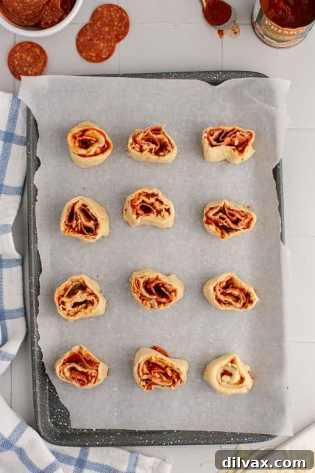 Cheesy Pepperoni Pizza Spirals 7 Pinwheels with pepperoni and pizza sauce ready to be baked on a baking sheet.