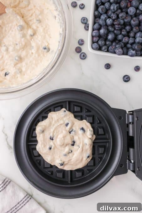 Pouring blueberry waffle batter into a preheated waffle iron.