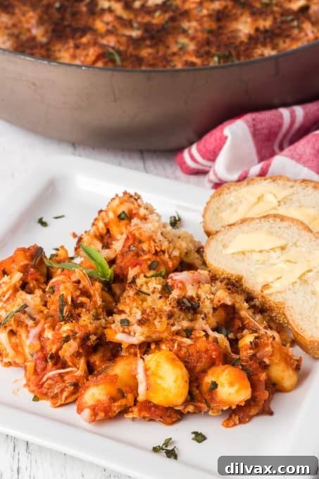 Gnocchi simmering in a rich chicken parmesan sauce in a skillet.