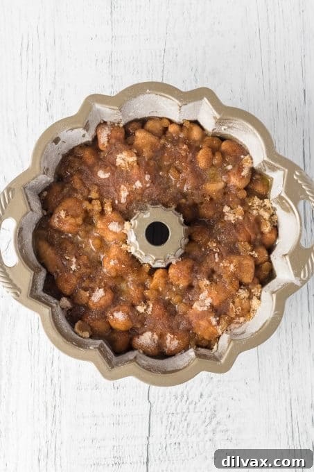 Moms Homemade Monkey Bread 7 Melted butter being spooned over brown sugar and dough pieces in a Bundt pan.