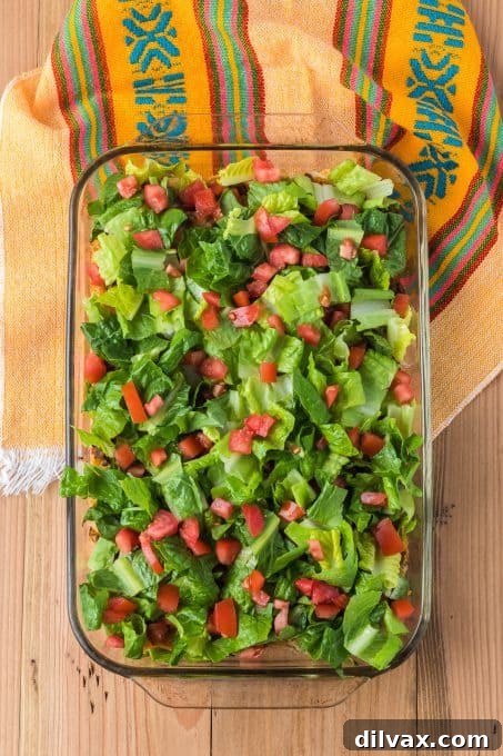 Taco casserole with fresh lettuce and tomatoes layered over seasoned beef and Fritos