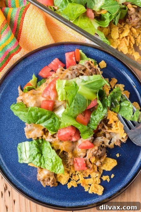 Layers of Fritos, seasoned ground beef, fresh lettuce, tomatoes, and melted cheese in a Taco Casserole
