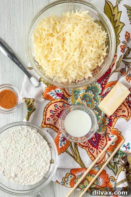 Handcrafted Cheesy Crisps 4 Key ingredients for homemade cheddar cheese crackers laid out on a surface, including cheese, cold butter, flour, and seasonings.