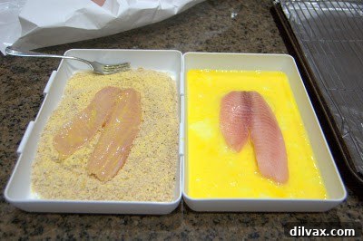 A tilapia fillet being coated with the breadcrumb mixture in a shallow dish.