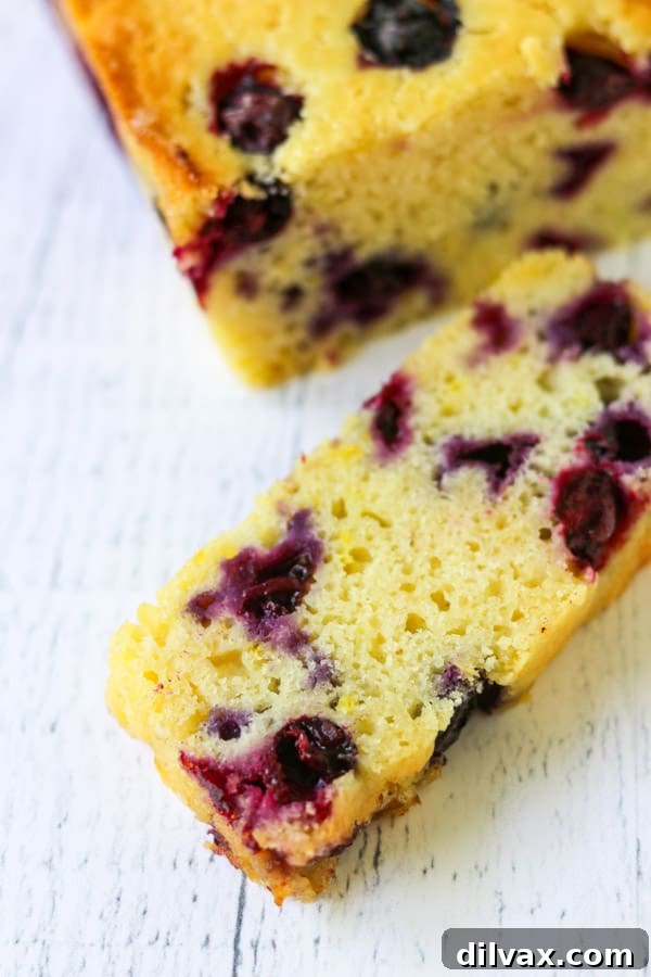 Close-up of a rustic loaf of Lemon Blueberry Bread on a cooling rack, highlighting the golden crust and plump blueberries within.
