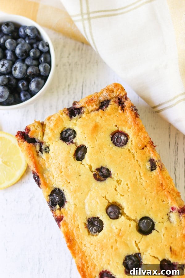 A slice of golden Lemon Blueberry Quick Bread on a white plate, showcasing the vibrant blueberries and inviting texture, ready to be enjoyed.