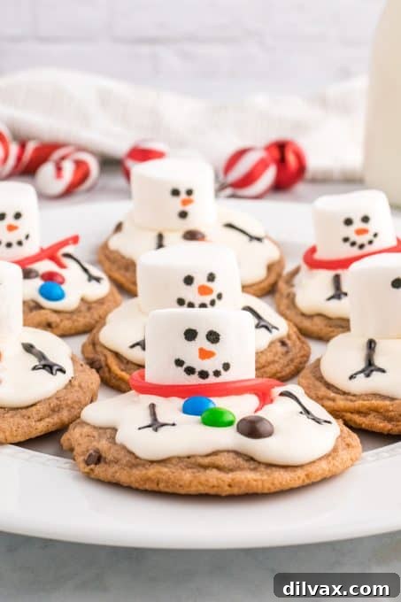 A close-up of a single melted snowman cookie, showcasing the marshmallow head with drawn features, a licorice scarf, and mini M&M buttons, all on a rich chocolate cookie base with soft marshmallow frosting that appears to be melting.