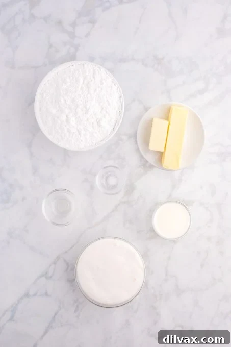 Ingredients for the marshmallow cream icing, including butter, a jar of Marshmallow Fluff, clear vanilla extract, and milk, displayed in a neat arrangement for easy viewing.