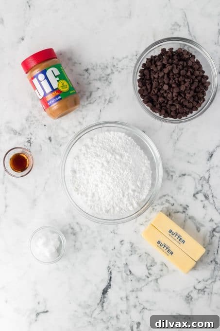 A selection of ingredients laid out on a wooden board, including a jar of peanut butter, butter sticks, powdered sugar, chocolate chips, and vanilla extract.
