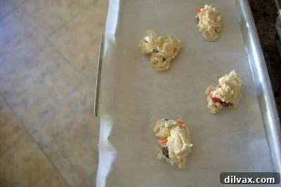 Scoops of M&M cookie dough placed on a parchment-lined baking sheet.