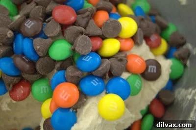 M&Ms and chocolate chips being stirred into cookie dough.