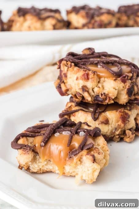 Golden Caramel Thumbprint Bites 12 A single Caramel filled cookie with a chocolate drizzle on a white plate, ready to be picked up and enjoyed.